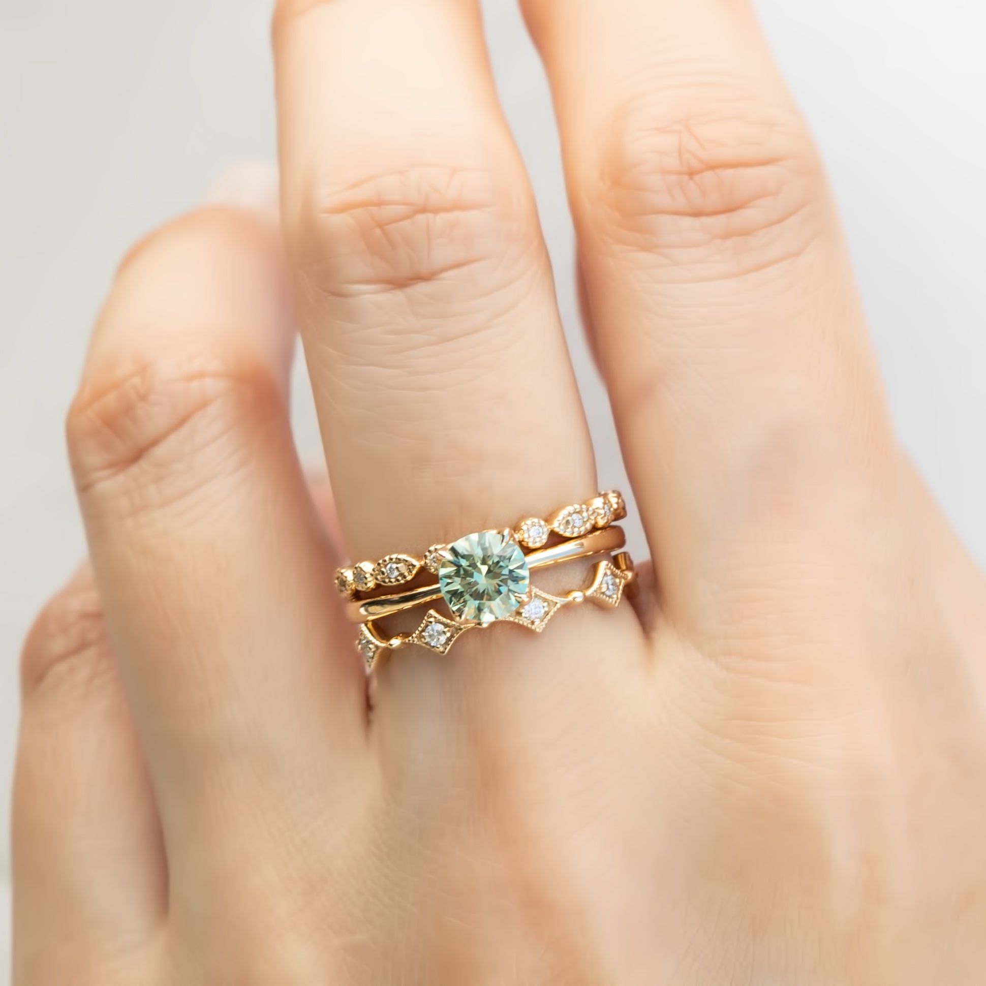 Close-up of hand wearing gold artisanal rings with diamonds featuring detailed milgrain and geometric design accents