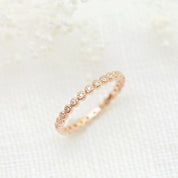 Rose gold Dahlia Diamond Eternity Ring with bezel-set natural white diamonds, displayed on a soft, light fabric background.