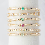 Stacked delicate 14k gold rings with various small gemstones on a white ring holder display.