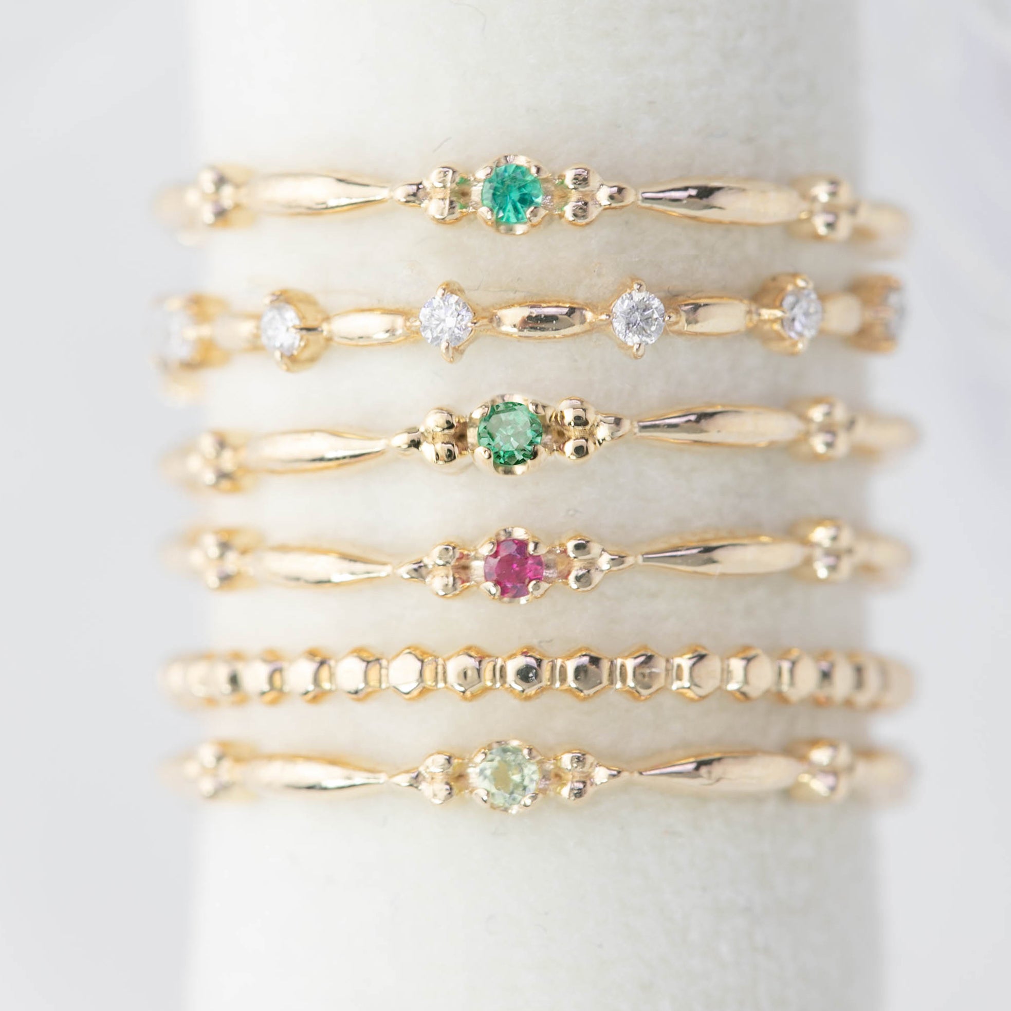 Stacked delicate 14k gold rings with various small gemstones on a white ring holder display.