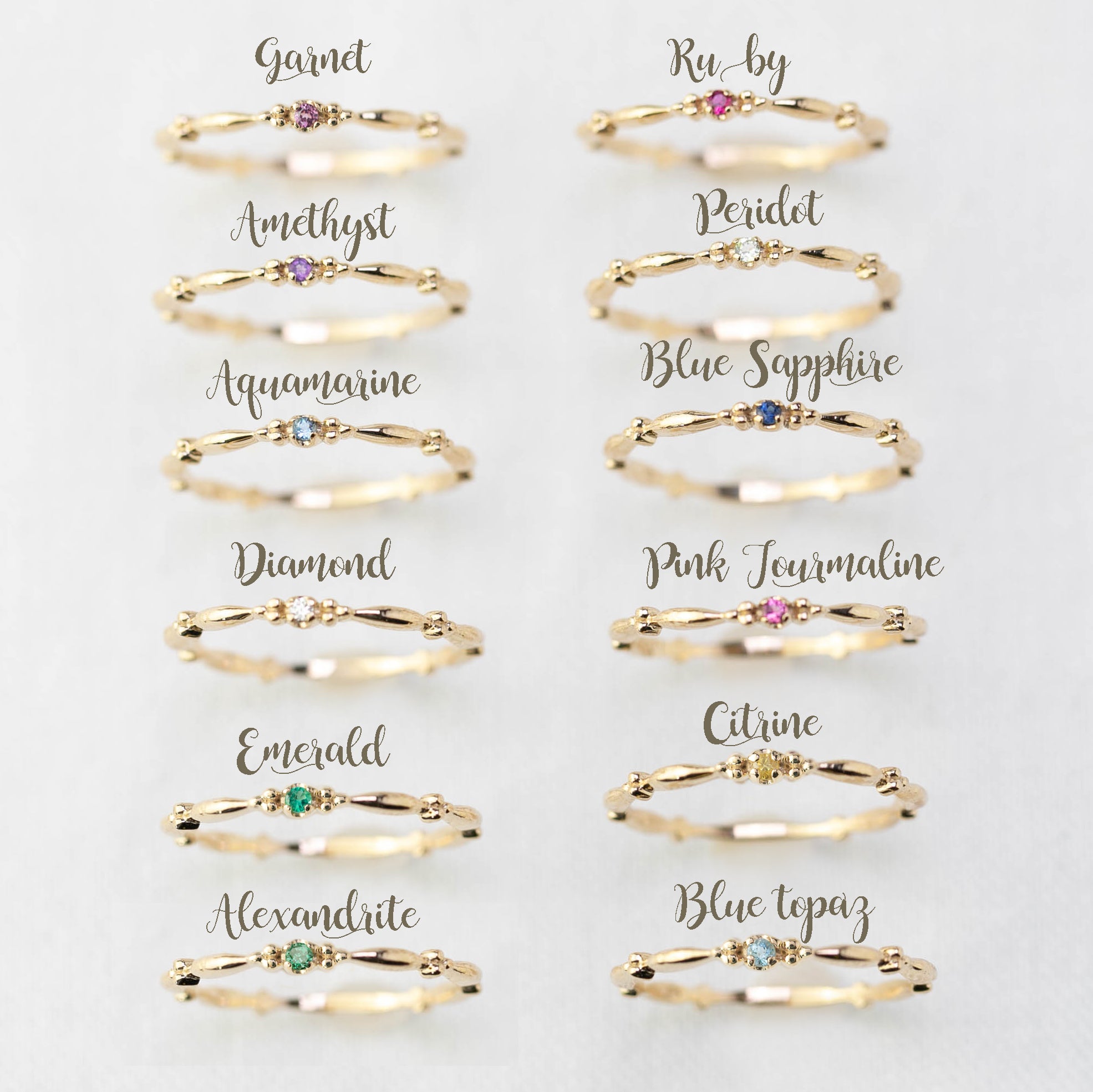 Twelve 14k gold birthstone rings including ruby, sapphire, emerald, diamond, garnet, amethyst, and others in size 7 displayed on white background.