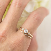 Hand wearing two gold rings with a brilliant-cut diamond and smaller accent diamonds in milgrain bezel settings