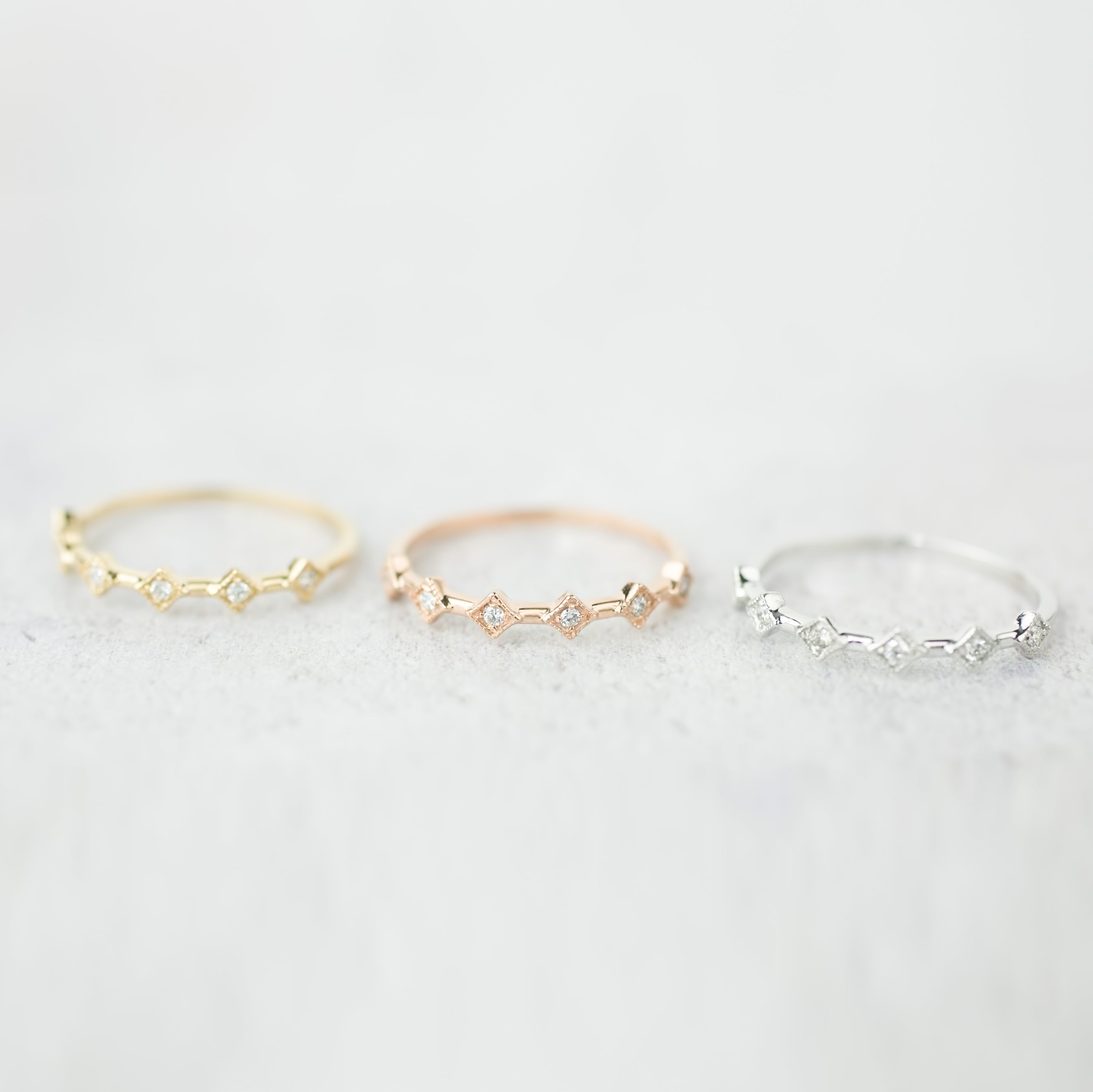 Three Six Star Rings in gold, rose gold, and silver with natural white diamonds on a soft gray background.