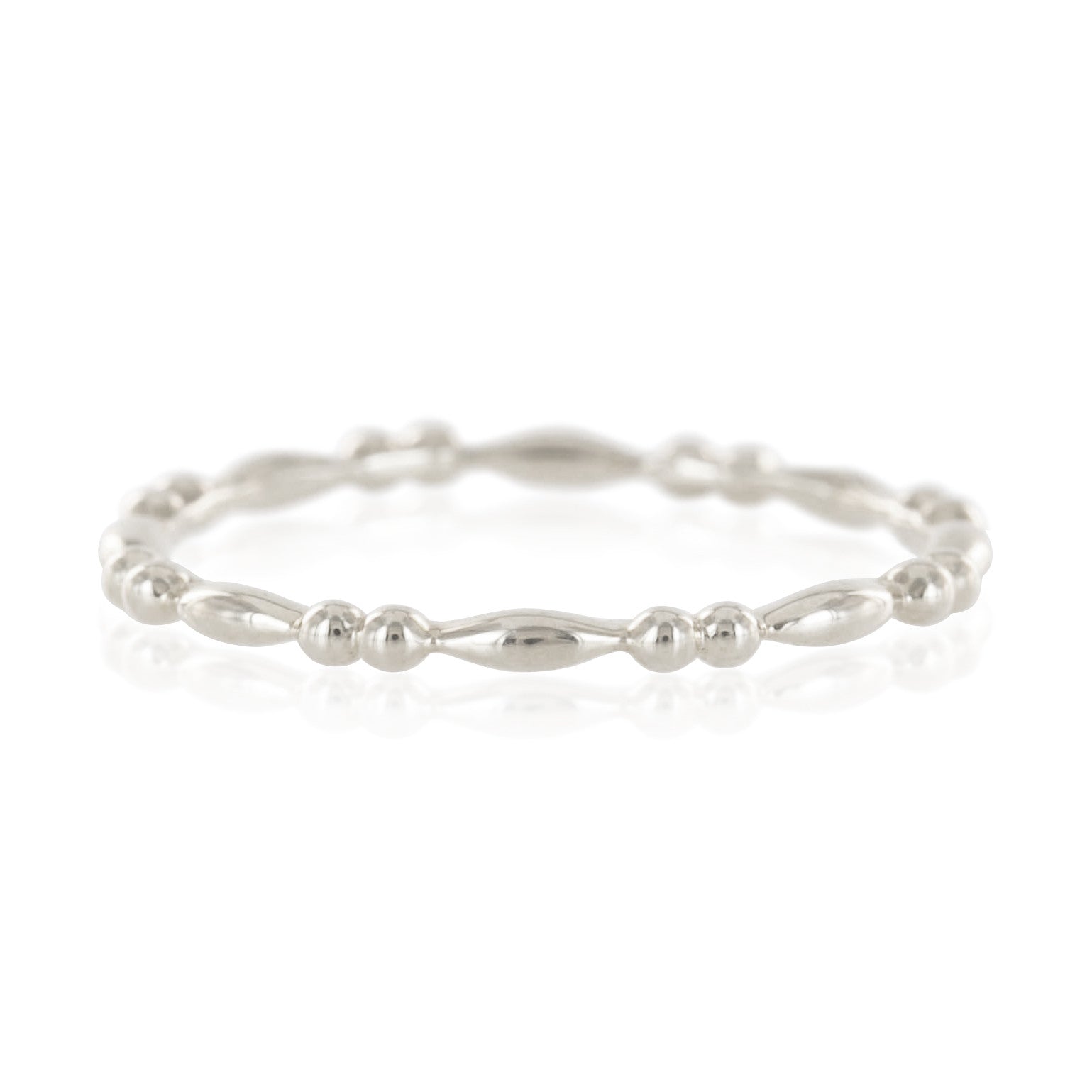 Close-up of a delicate beaded silver eternity ring with alternating small round and elongated beads on a white background