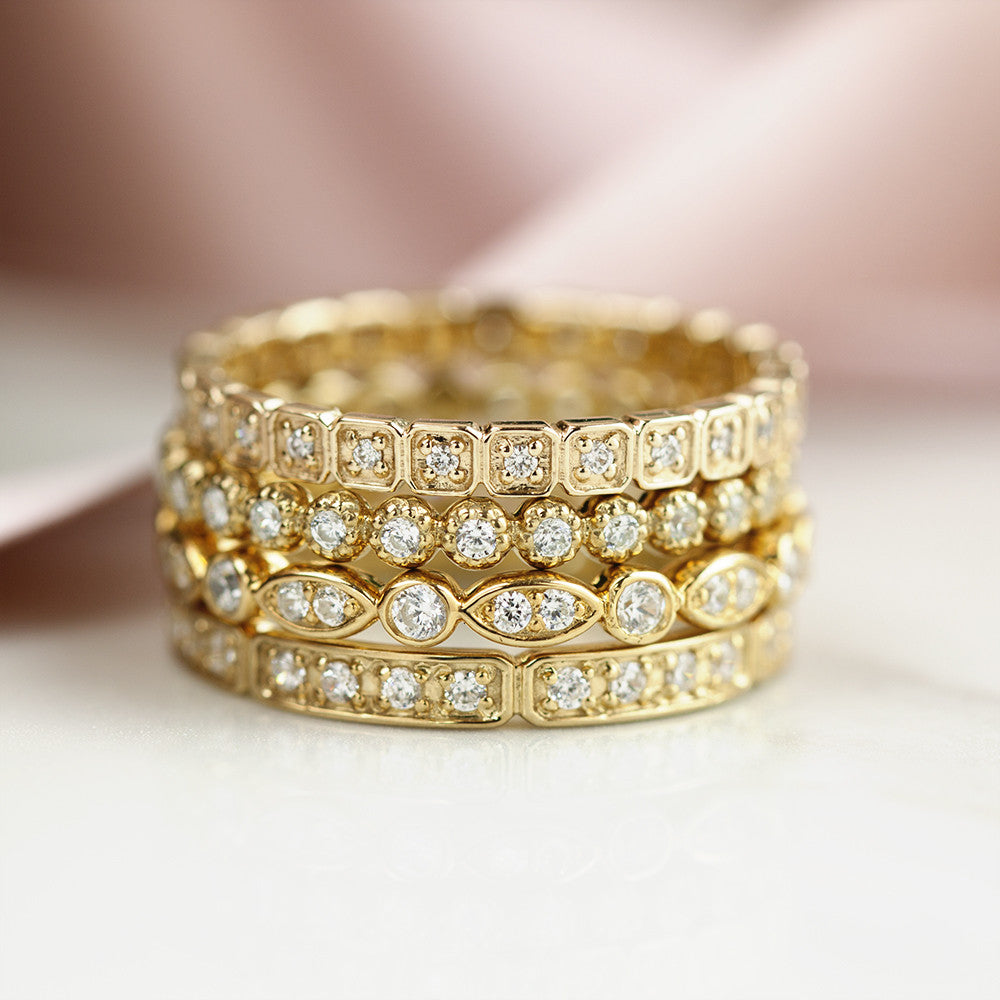 Stack of four gold eternity rings with natural white diamonds in various settings on a neutral background