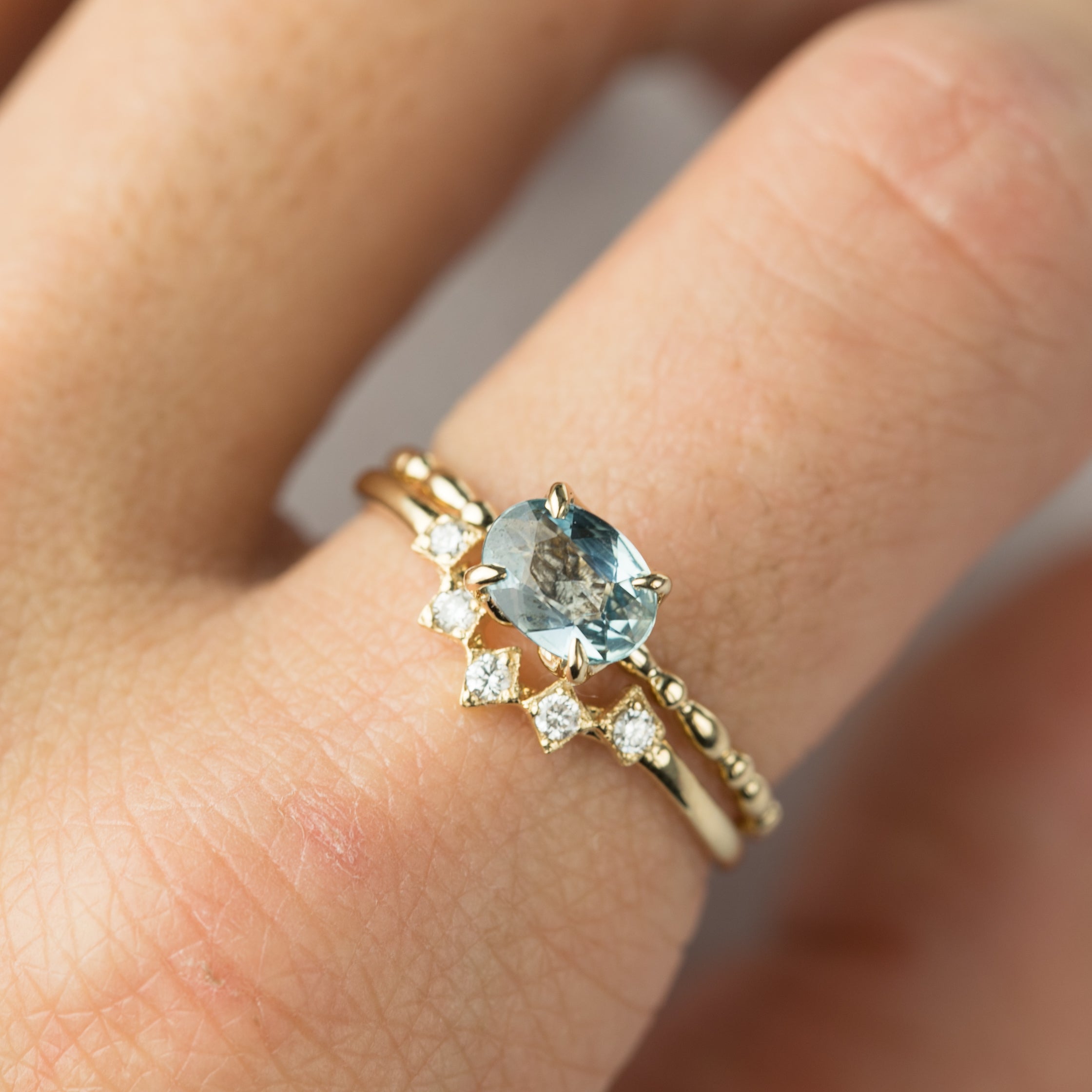 Close-up of a hand wearing a gold star tiara ring with a blue gemstone and small white diamonds in a V-shaped band.