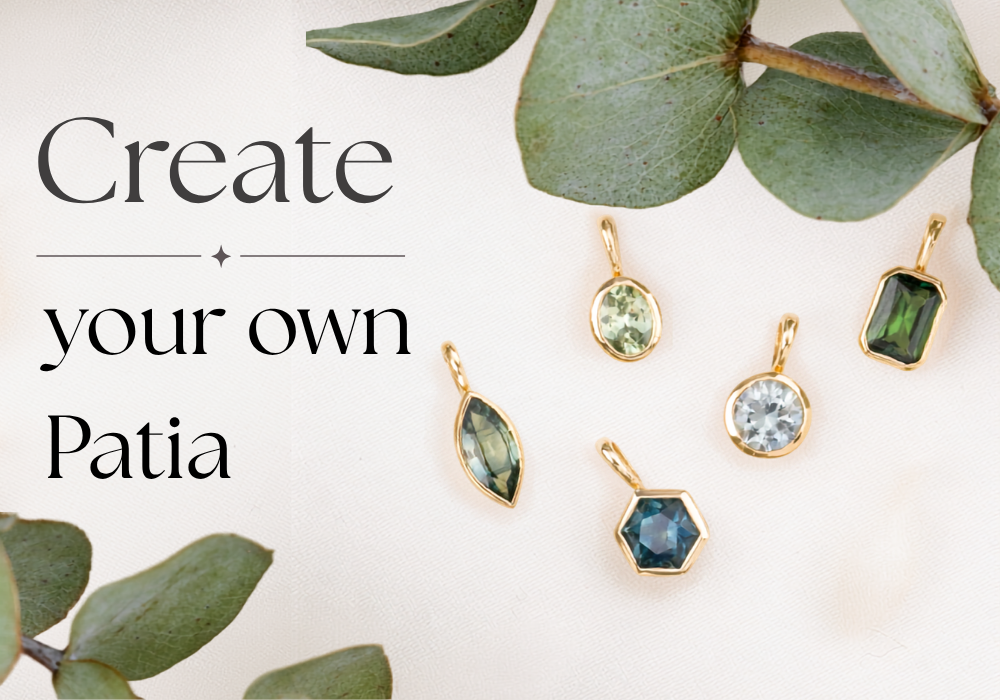 Five gold pendant charms with different colored gemstones are arranged on a light cream background with green eucalyptus leaves. The text on the left reads 'Create your own Patia'.