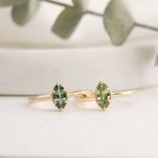 Two gold rings with green gemstones on a light lifestyle background