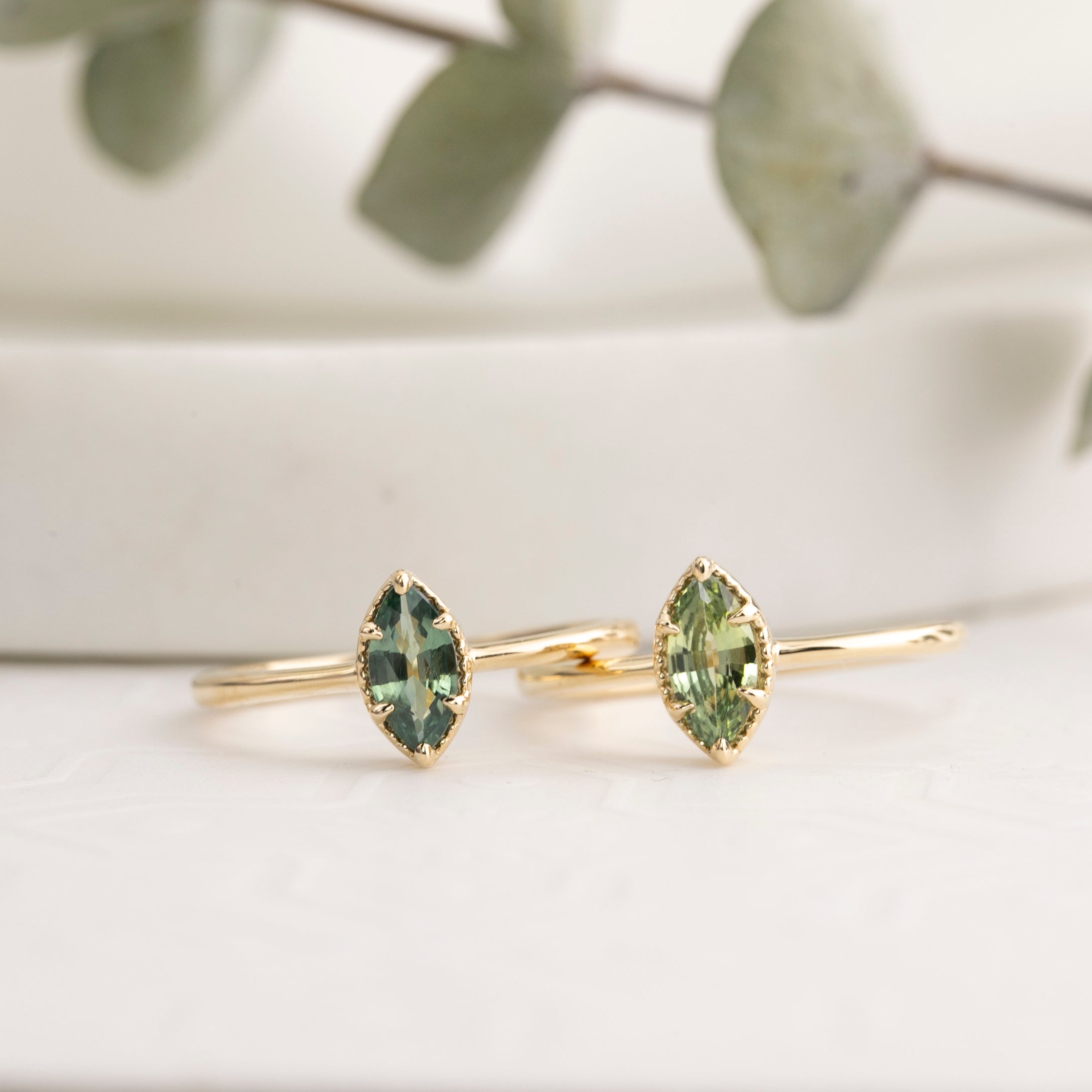 Two gold rings with green gemstones on a light lifestyle background