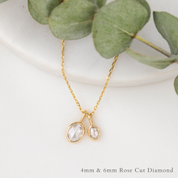 Gold necklace with rose cut diamonds on a white surface with eucalyptus leaves.