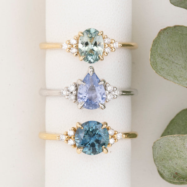 Three gold rings with different colored gemstones on a white surface with green leaves.