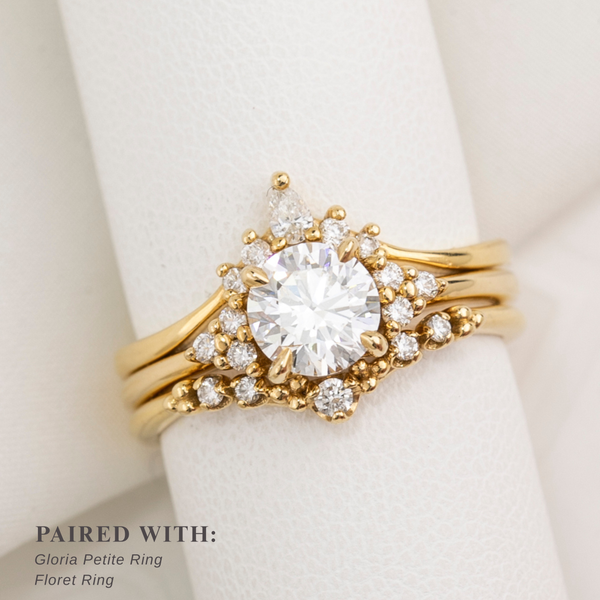 Gold ring with diamonds on a white surface, paired with other rings.
