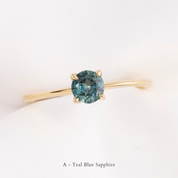 Gold ring with a teal blue sapphire on a light background