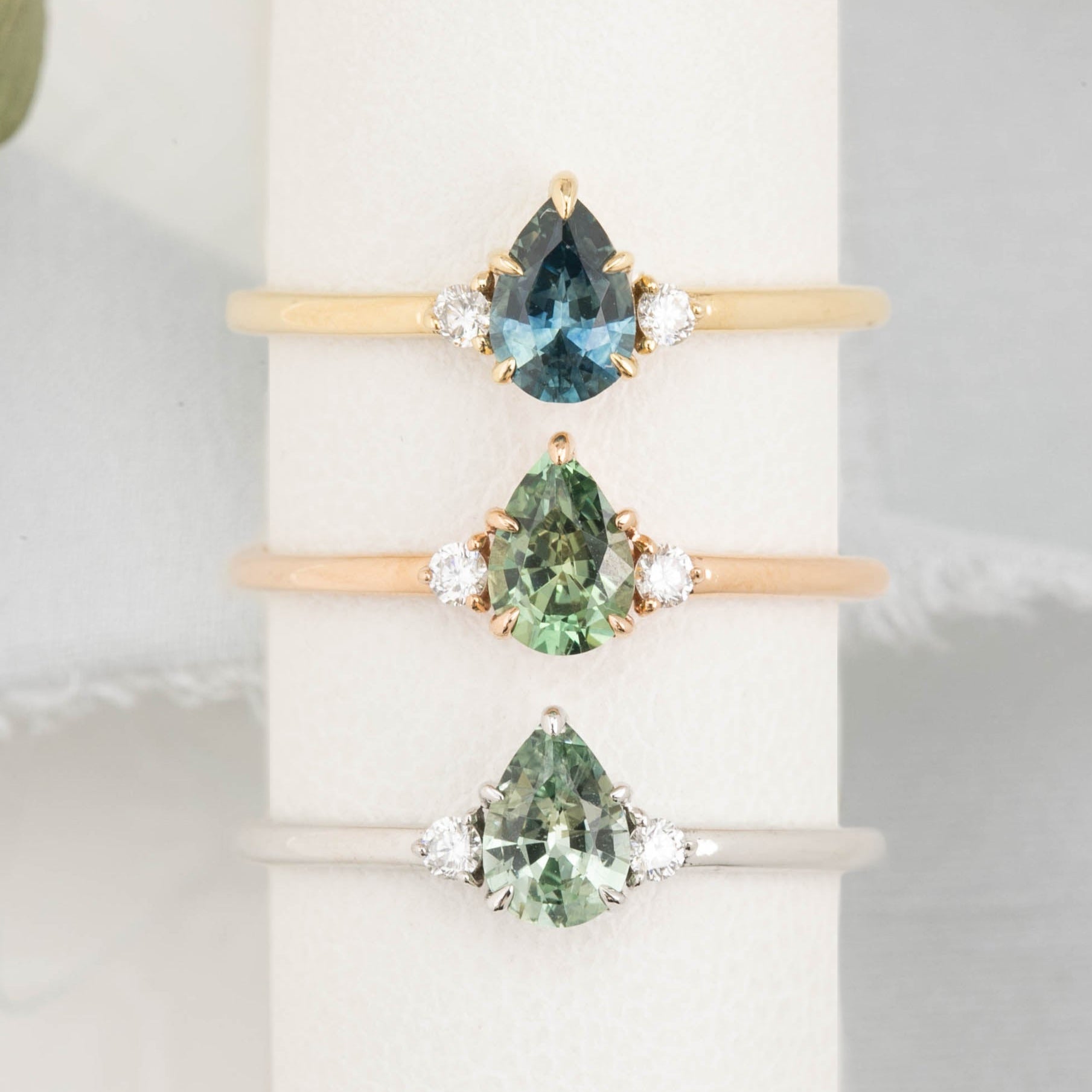 Three gold rings with pear-shaped sapphire in 14k yellow gold, rose gold and white gold