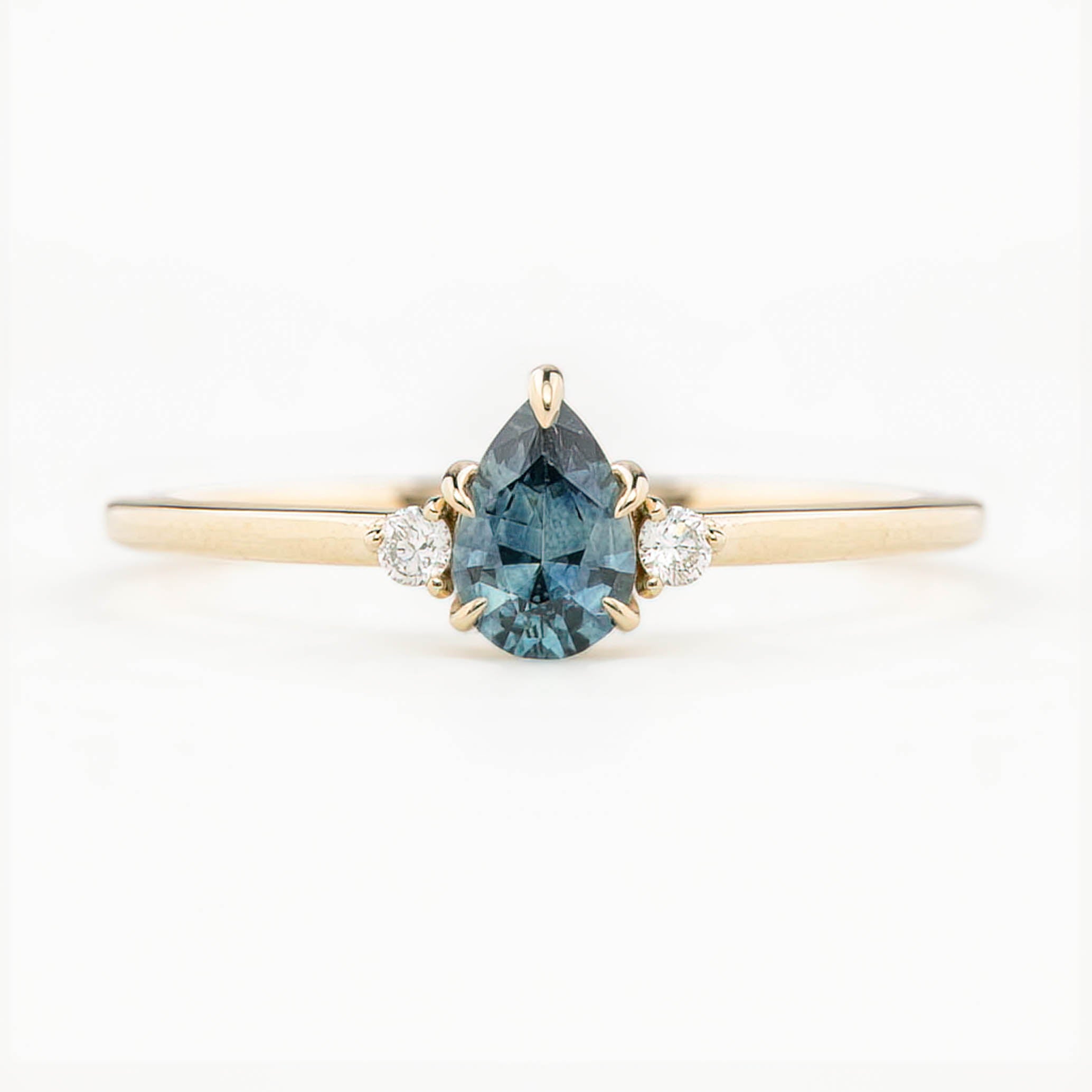 A pear-cut teal Montana sapphire ring with accent diamonds set in a 14k yellow gold band, displayed against a white background.