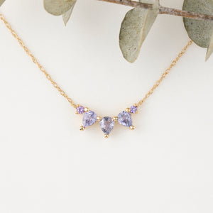 Gold necklace with purple gemstones on a white background