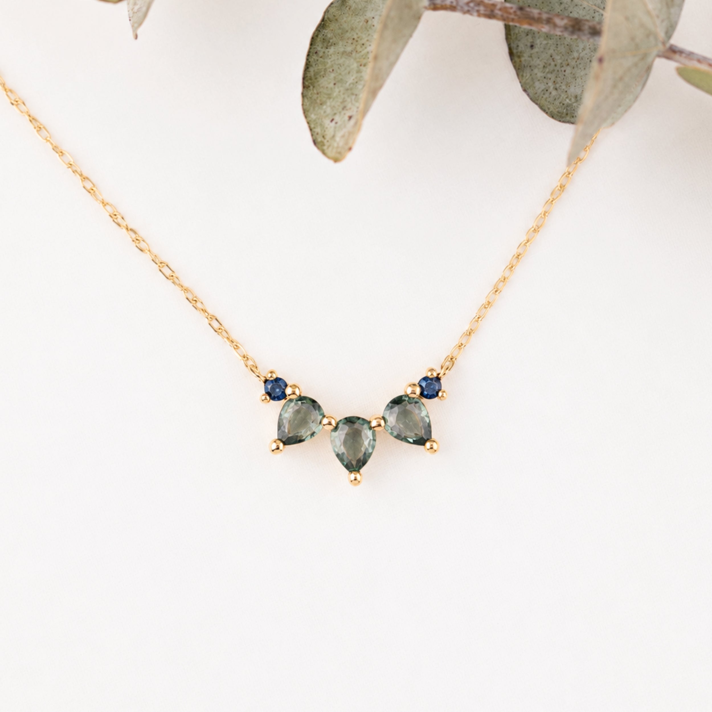 Gold necklace with green gemstones on a white background