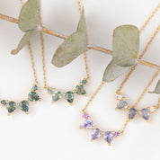 Gold necklaces with green and purple gemstones on a white background with eucalyptus leaves.
