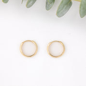 12mm Gold hoop earrings on a white background with green leaves.