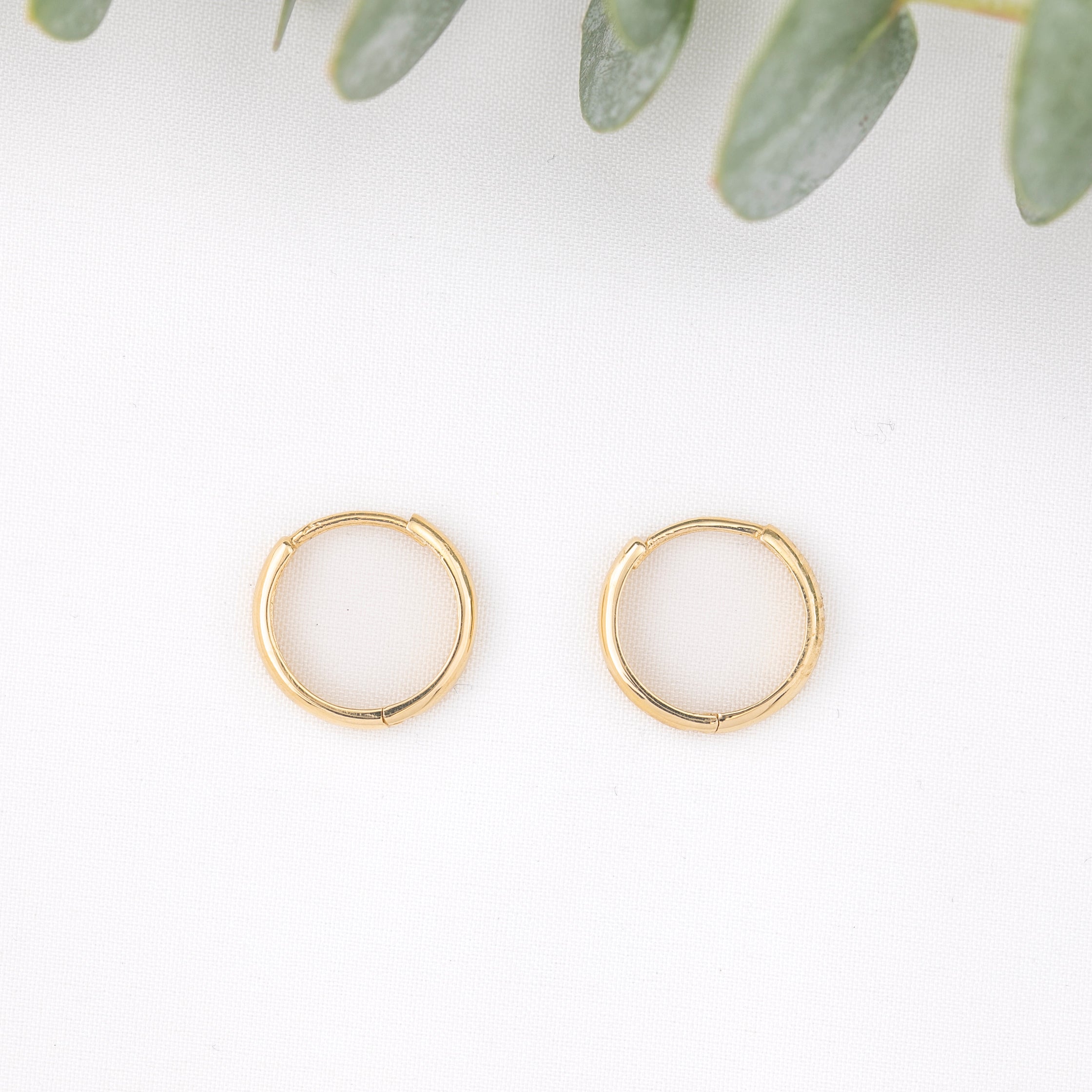 12mm Gold hoop earrings on a white background with green leaves.