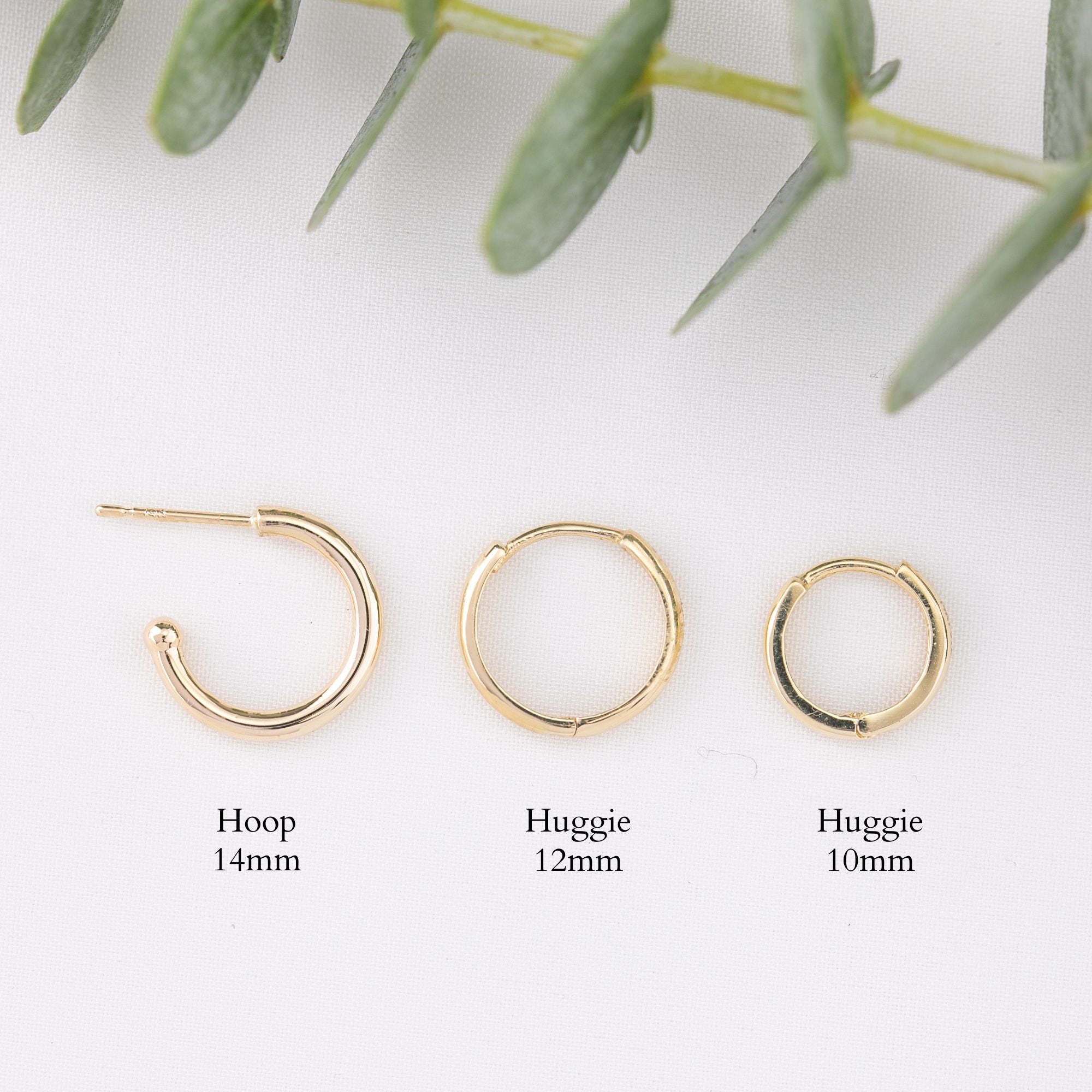 Three gold hoop earrings shown on a white background with green leaves at the top and size labels below: hoop 14mm, huggie 12mm, and huggie 10mm.