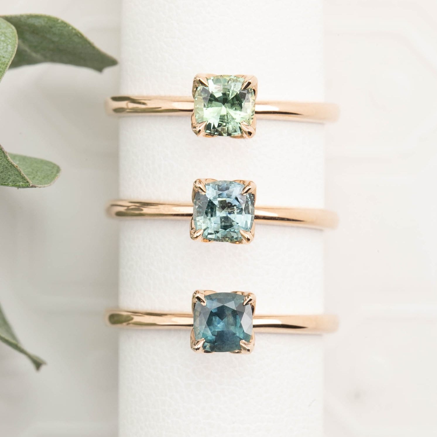 Three rose gold rings with square green gemstones on a white surface.