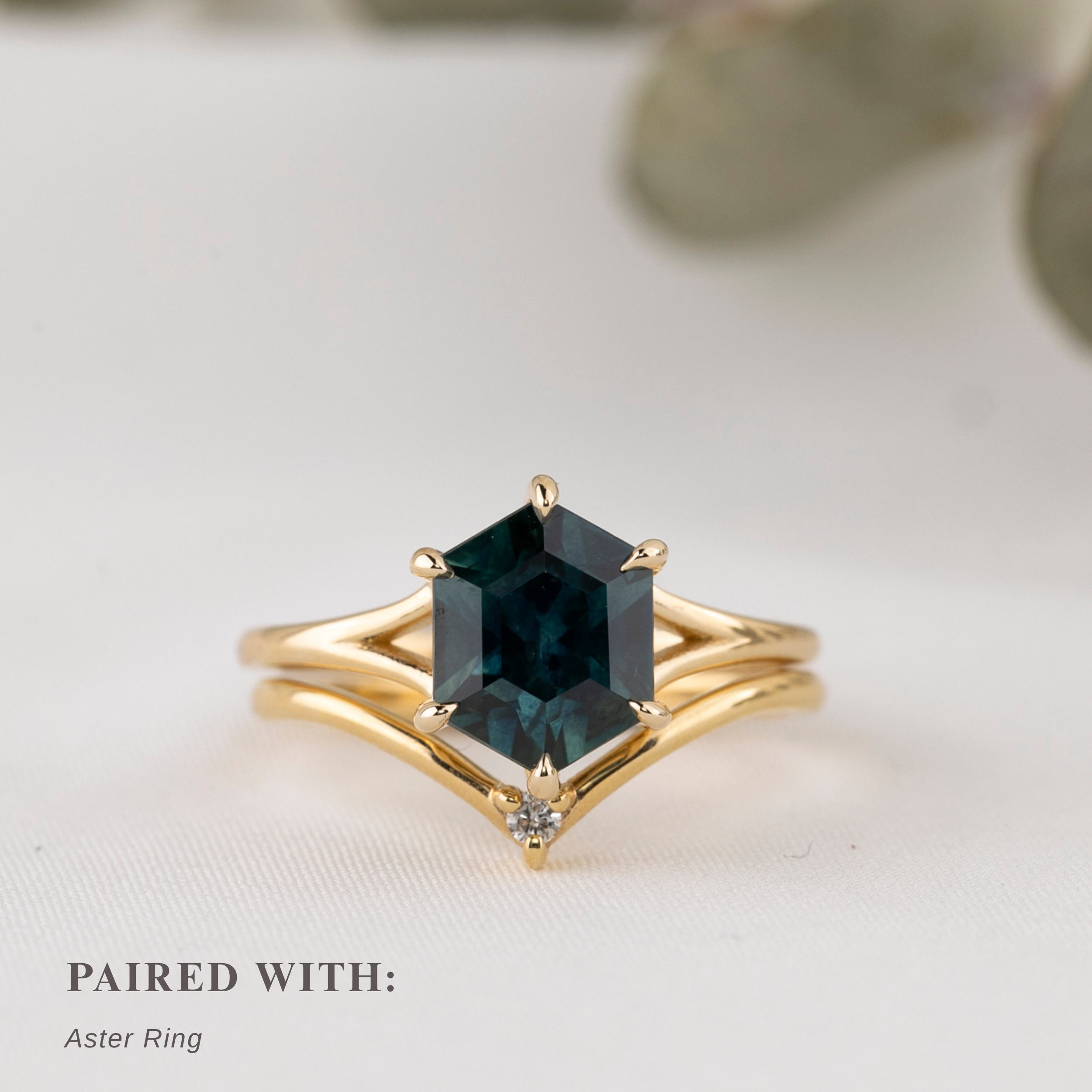 Gold ring with a green gemstone on a light background stacked withgold curve ring