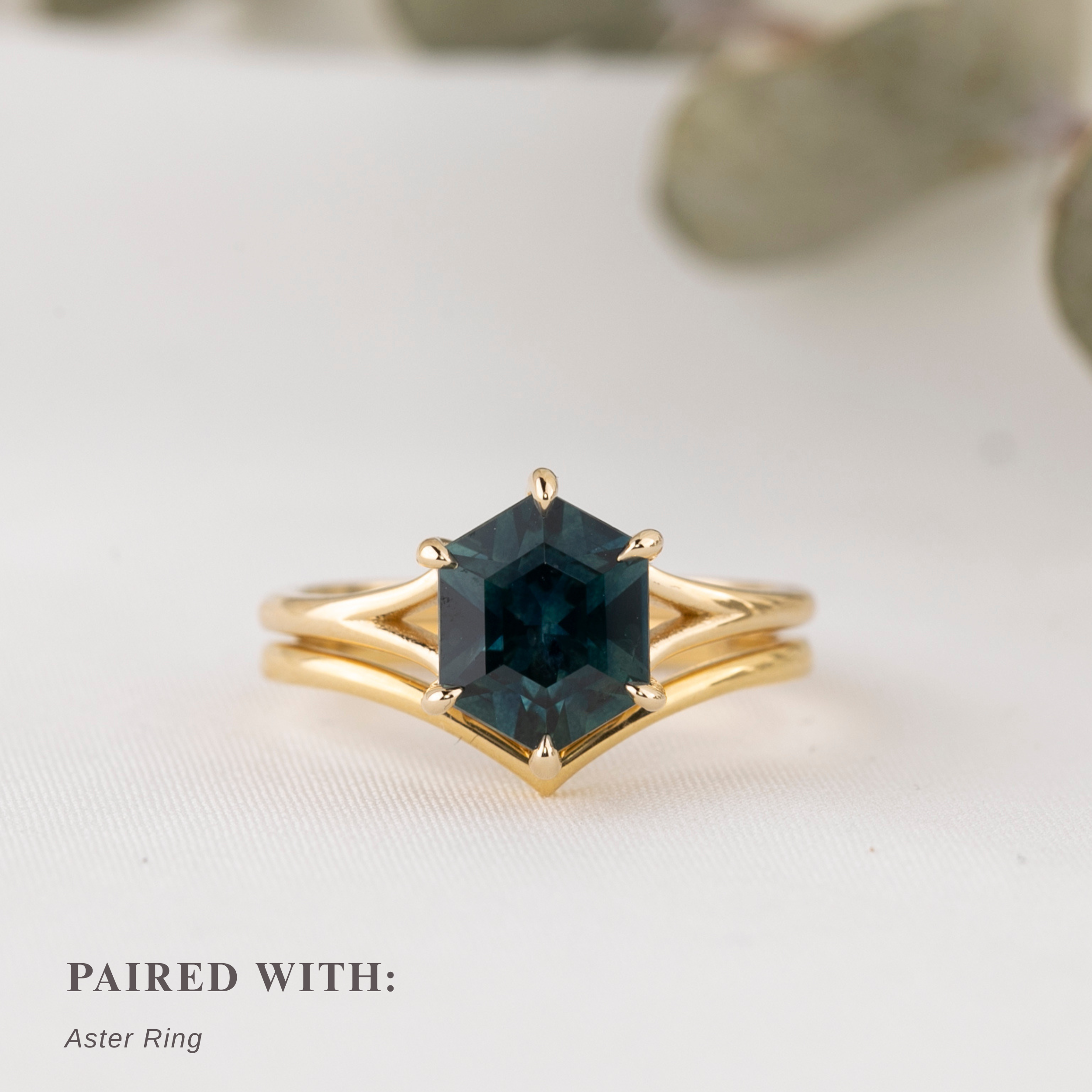Gold ring with a green gemstone on a light background stacked with plain gold curved ring