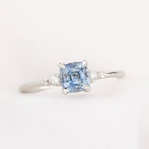 white gold ring with blue light blue cushion cut montana sapphire, with two natural accent diamonds on white background