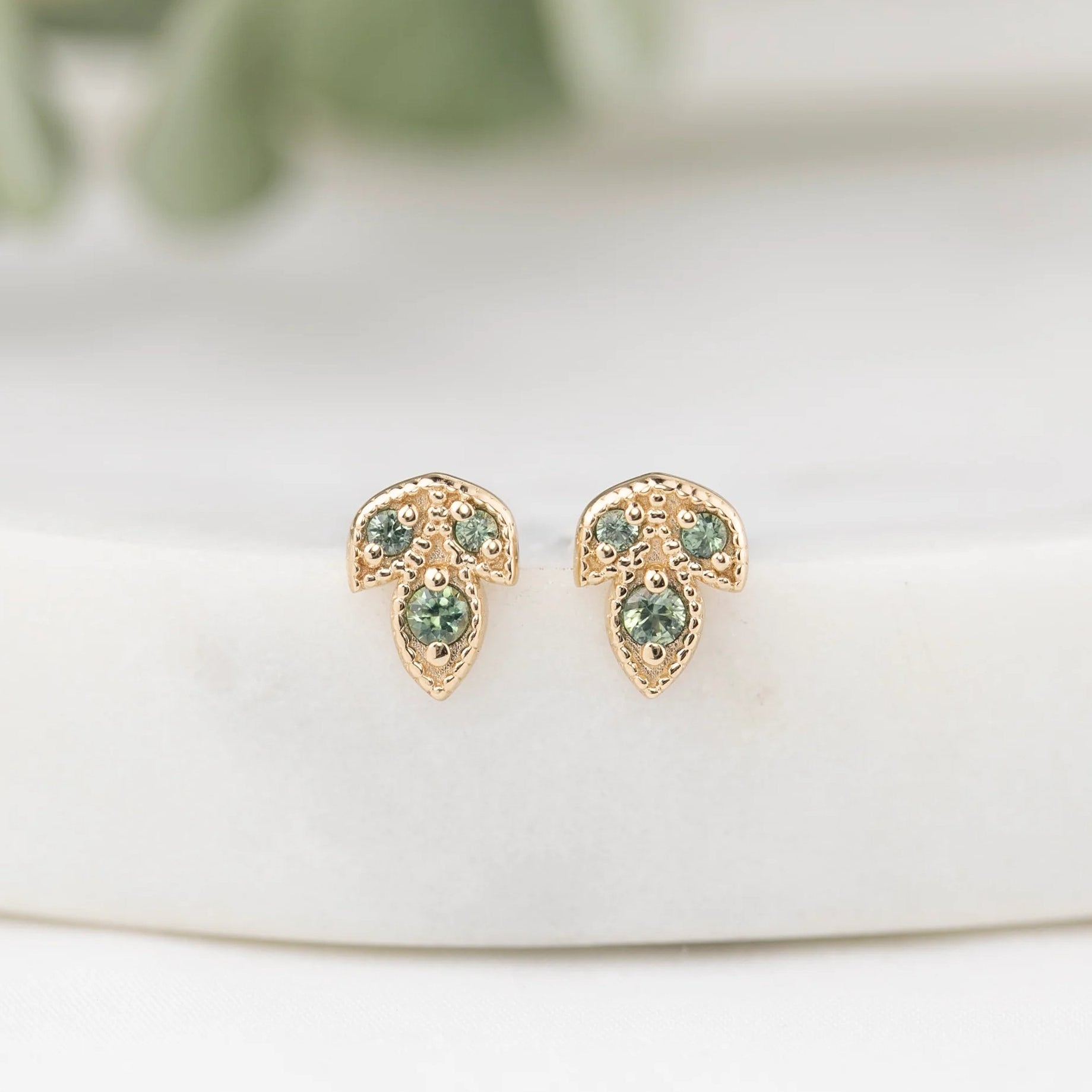 Gold earrings with green gemstones on a white surface