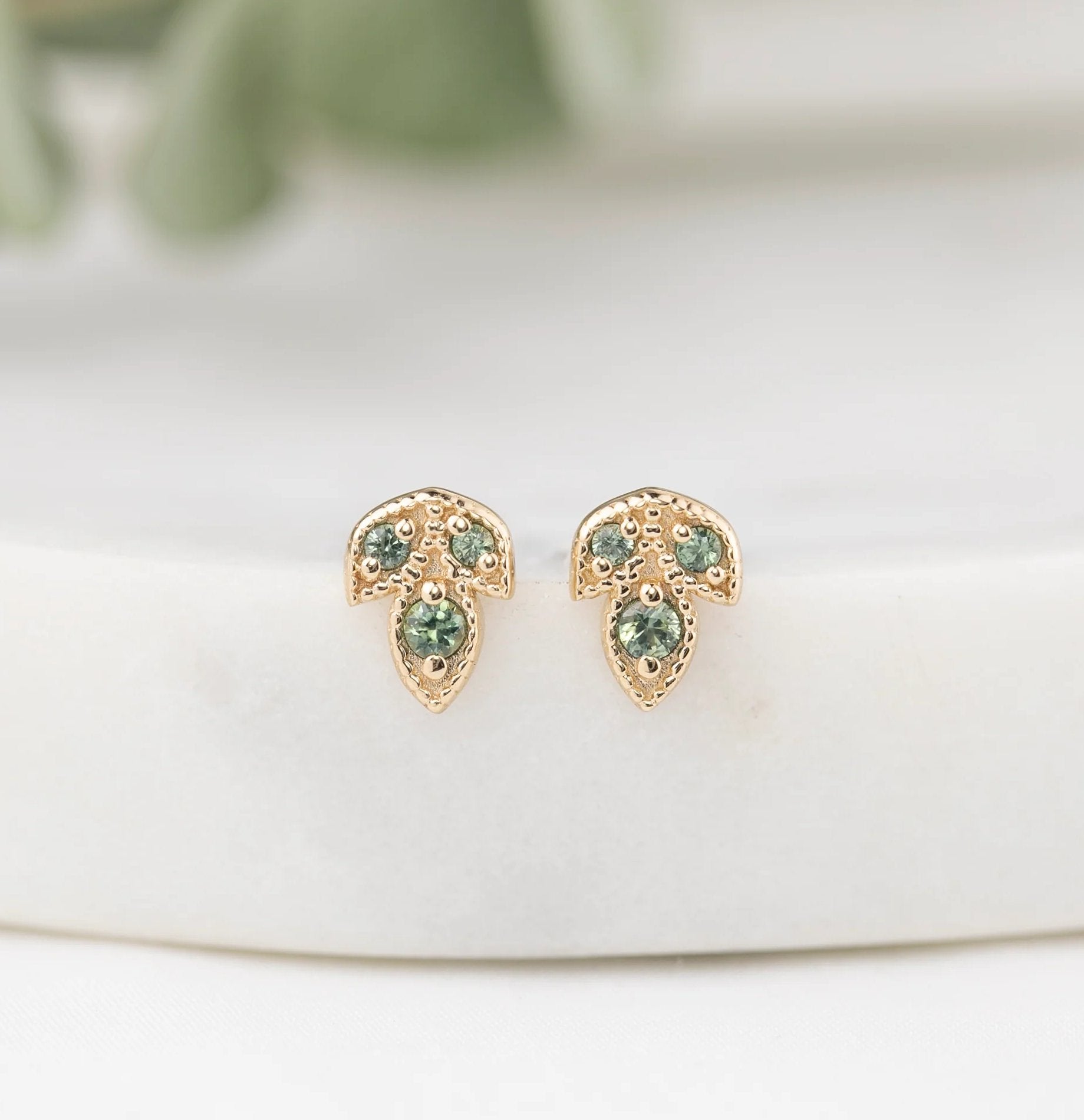 Gold earrings with green gemstones on a white surface
