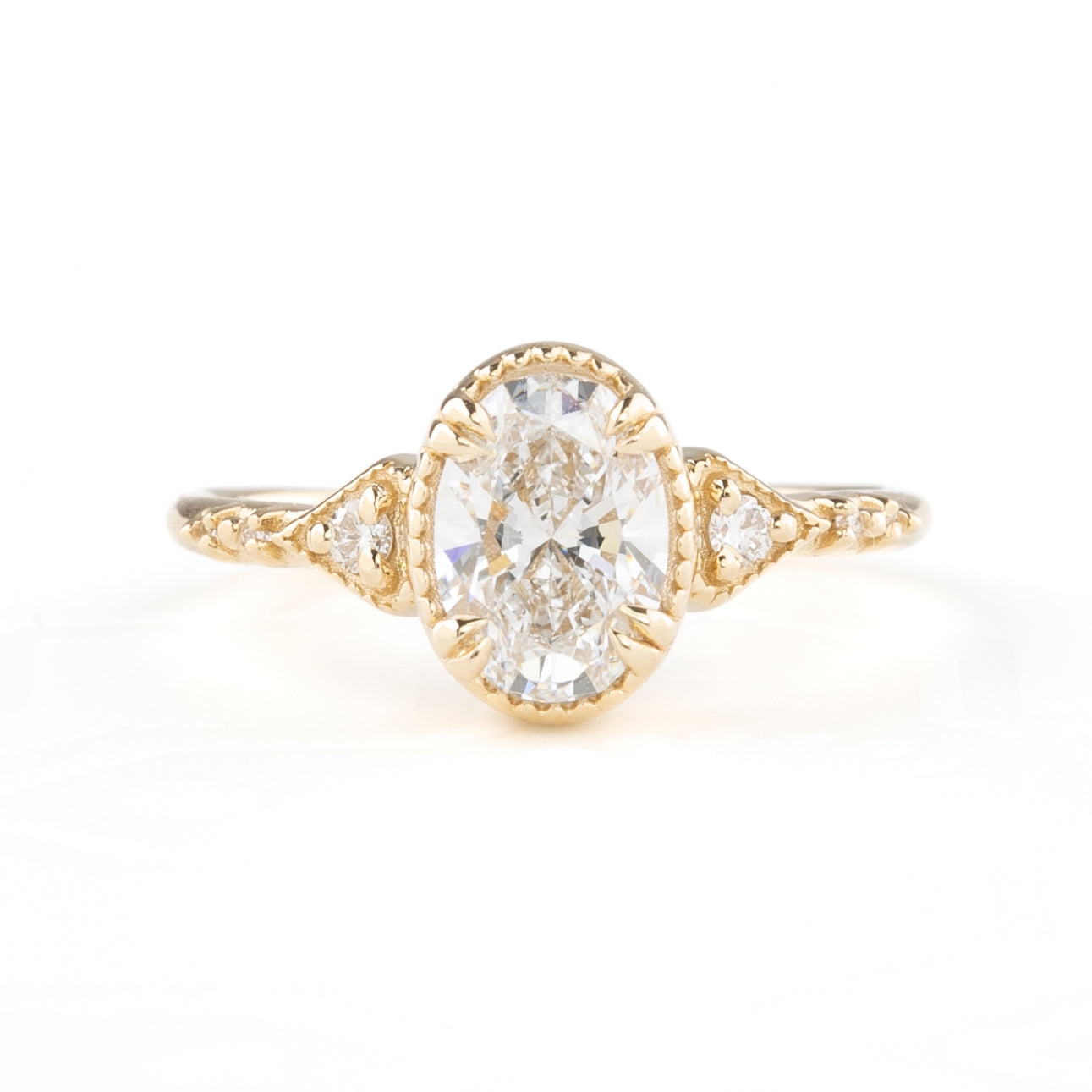 A golden ring featuring a central oval-shaped brilliant cut diamond with six smaller accent diamonds around it, set in a low-profile four double claw prong setting.
