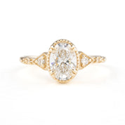 A golden ring featuring a central oval-shaped brilliant cut diamond with six smaller accent diamonds around it, set in a low-profile four double claw prong setting.