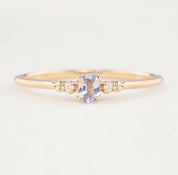 Gold ring with a central purple gemstone and smaller diamonds on a light background
