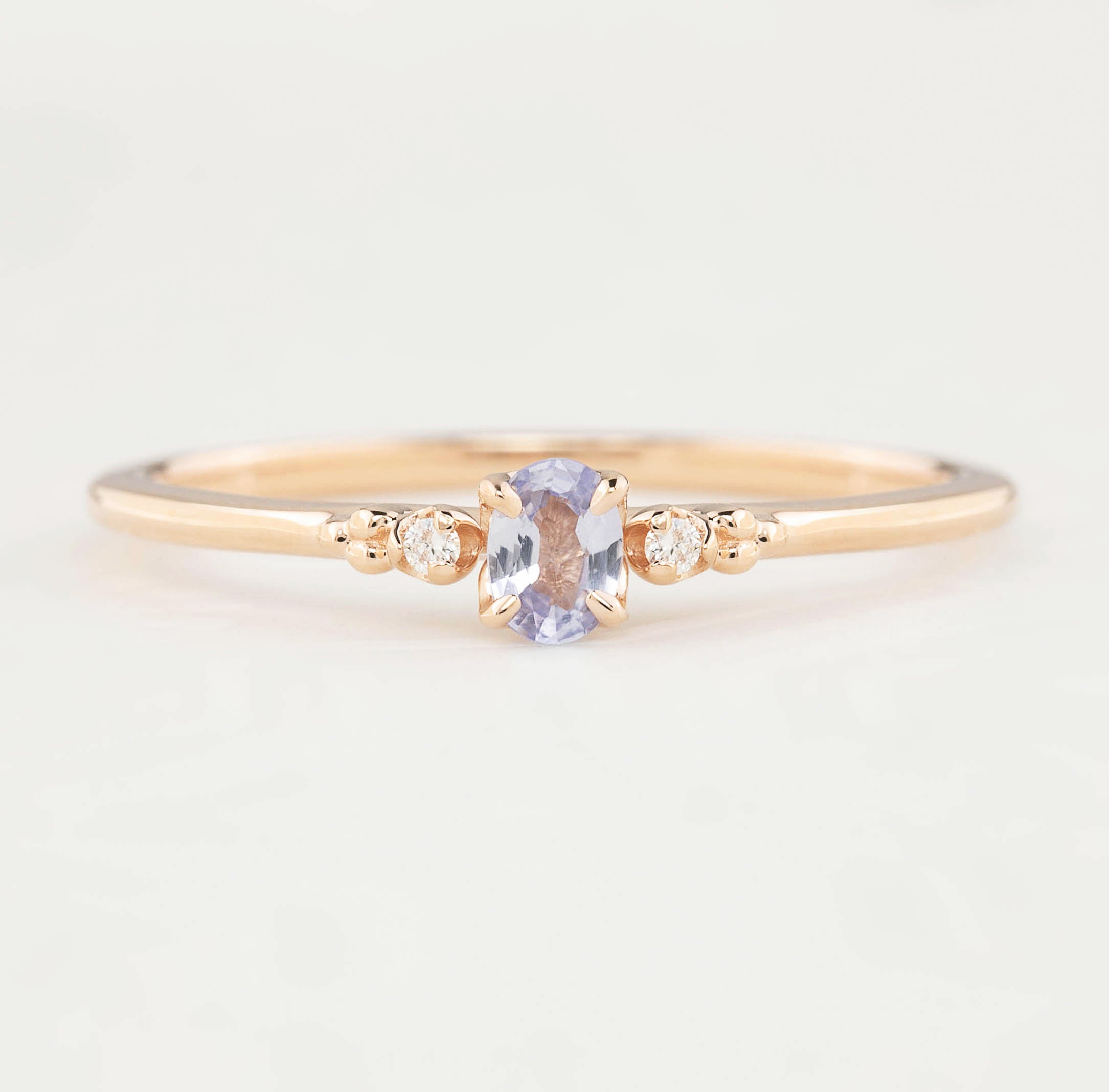 Gold ring with a central purple gemstone and smaller diamonds on a light background