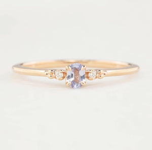 Gold ring with a central purple gemstone and smaller diamonds on a light background