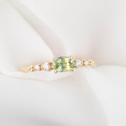 Gold ring with a green gemstone and smaller diamonds on a white fabric background