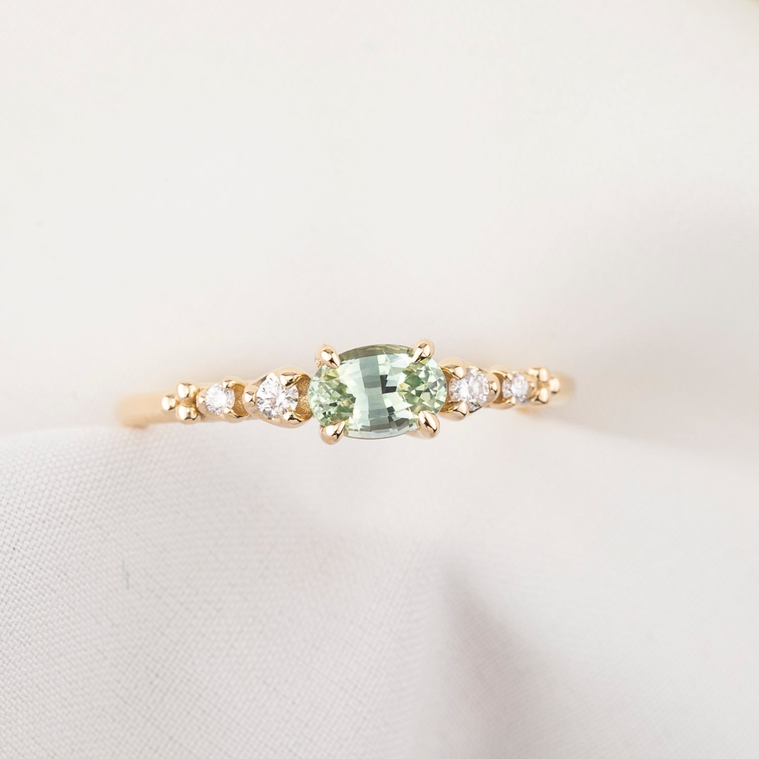 Gold ring with a green gemstone and smaller diamonds on a light background