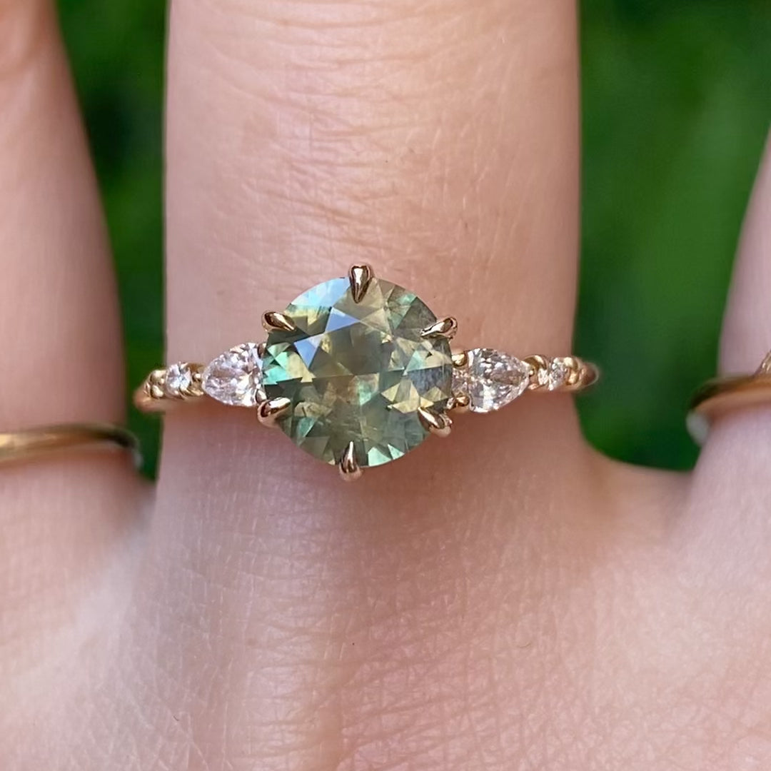 Video of Estel Fleur Petal Ring with a 1.53ct round green Montana sapphire and diamond accents in 14k yellow gold on a finger.