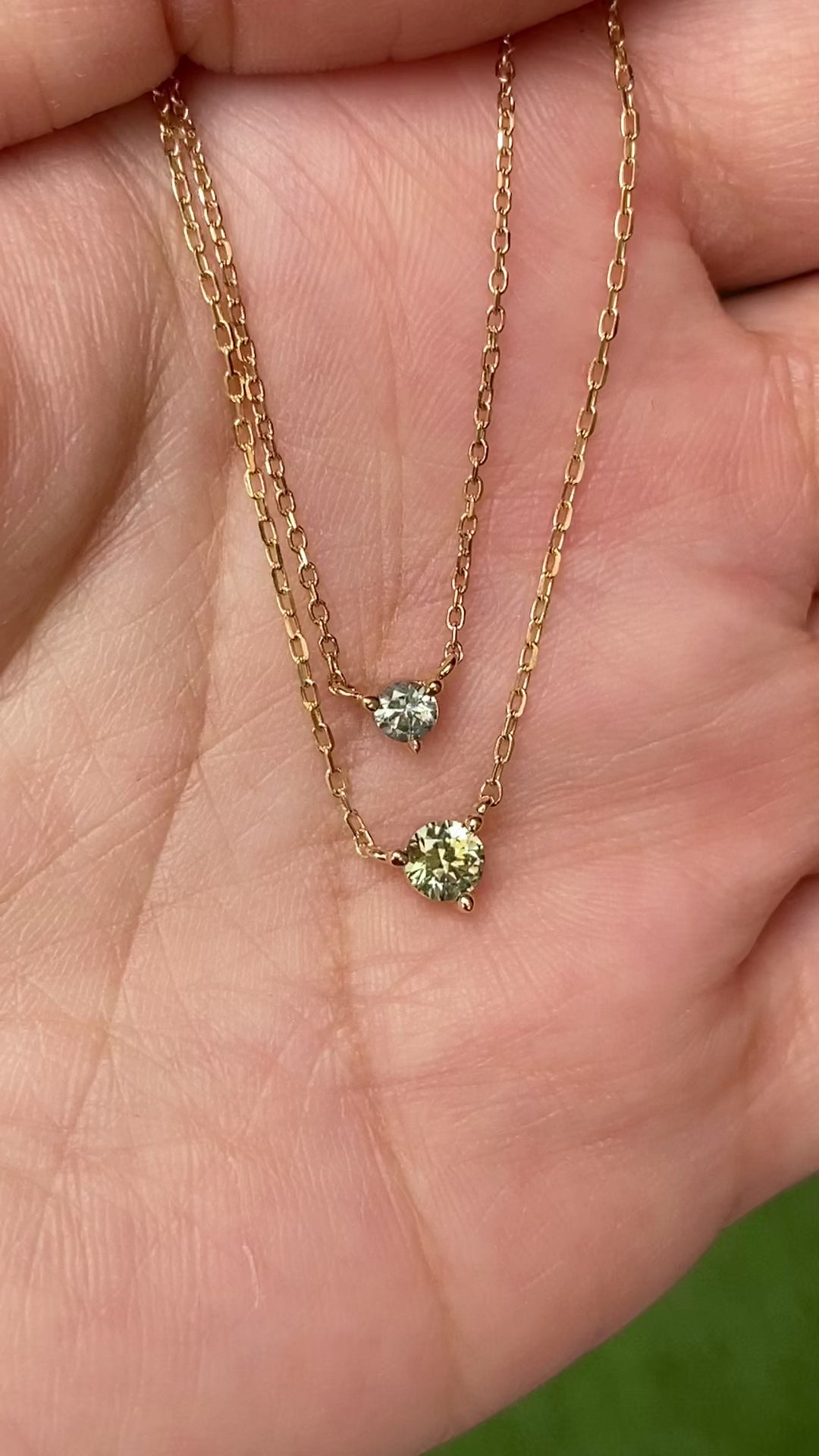 Comparison of 3.0mm Light Blue Green Sapphire Pendant Necklace next to 4.0mm Green Sapphire Pendant Necklace in 14k yellow gold in natural lighting