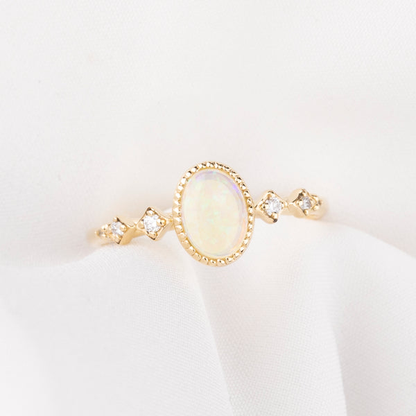Gold ring with a central opal stone and smaller diamonds on a white background
