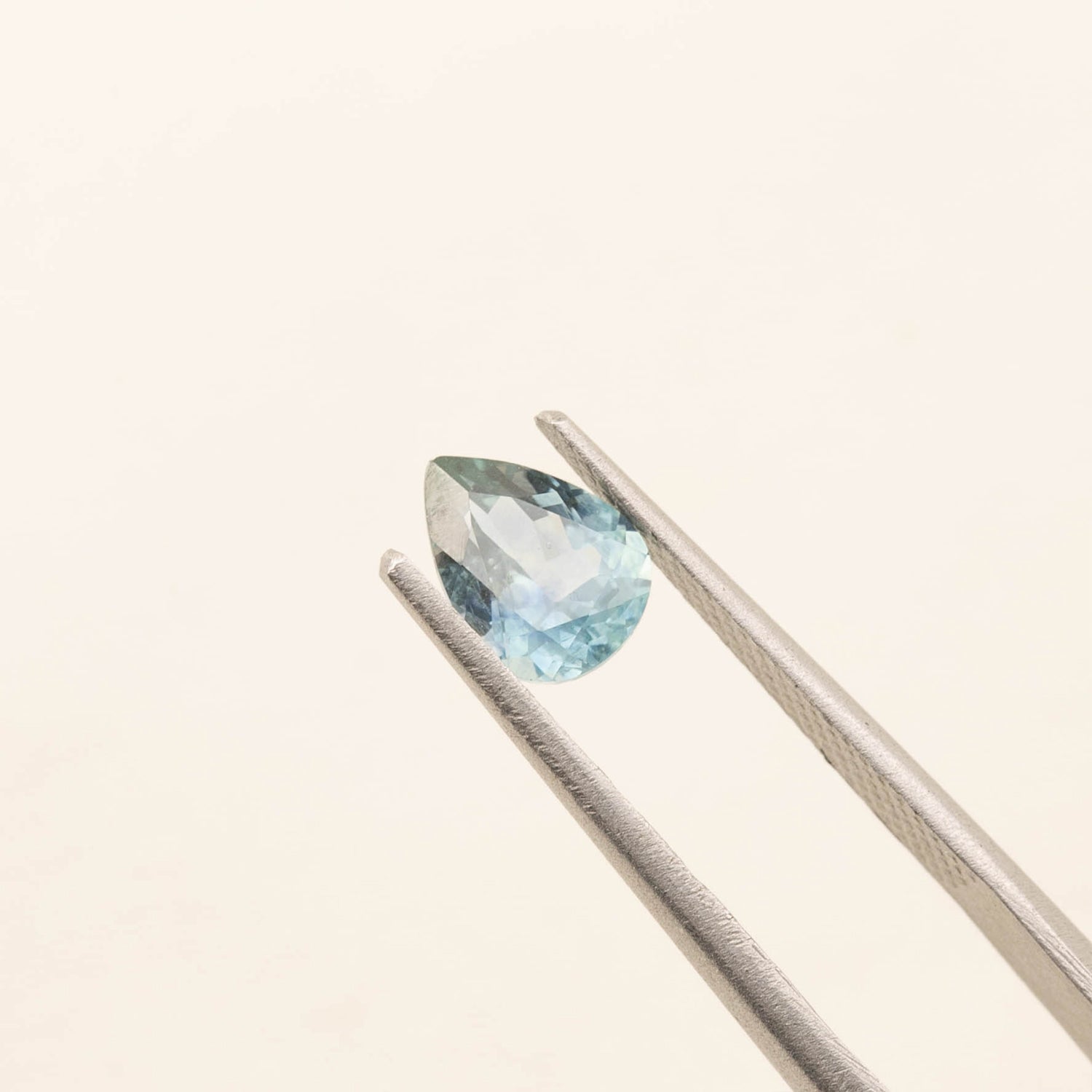 1.41ct pear-shaped Montana sapphire in blue-green held by tweezers on a light background