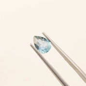 1.41ct pear-shaped Montana sapphire in blue-green held by tweezers on a light background