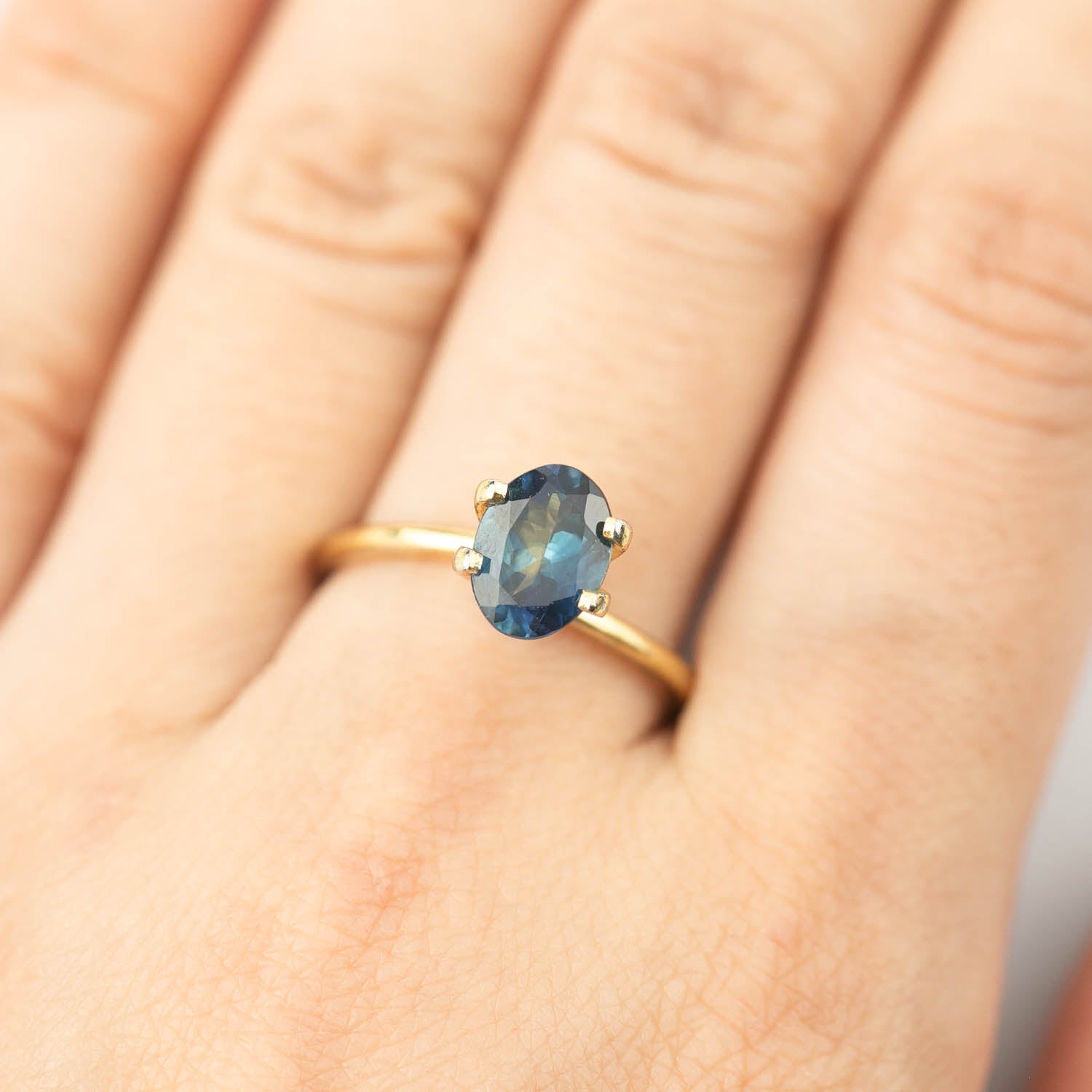 1.62ct oval cut teal blue Montana sapphire ring on finger with gold band, eye clean with small inclusions visible