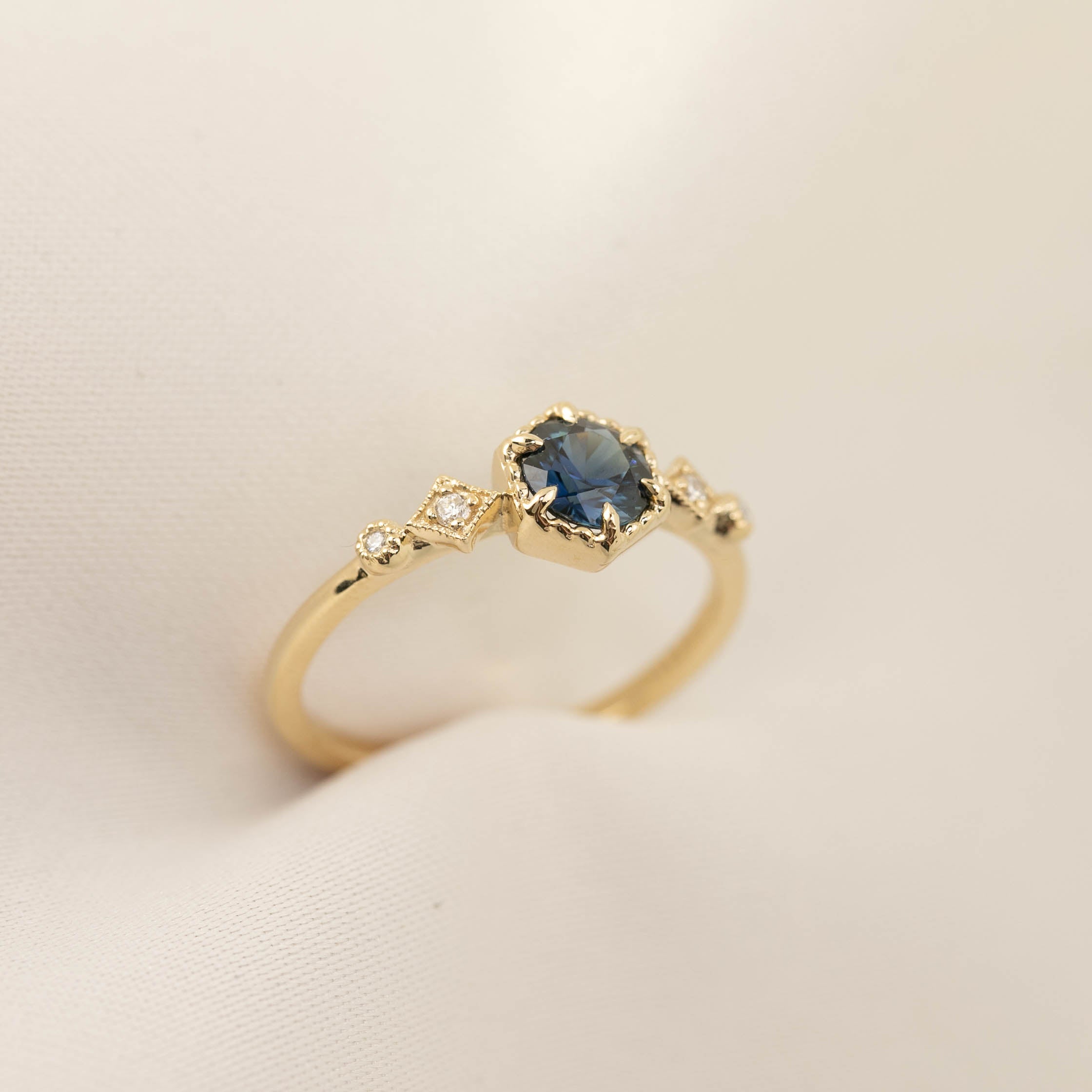 Delicate 14k gold ring featuring a 0.7ct Queensland peacock sapphire with accent diamonds in a bezel setting.