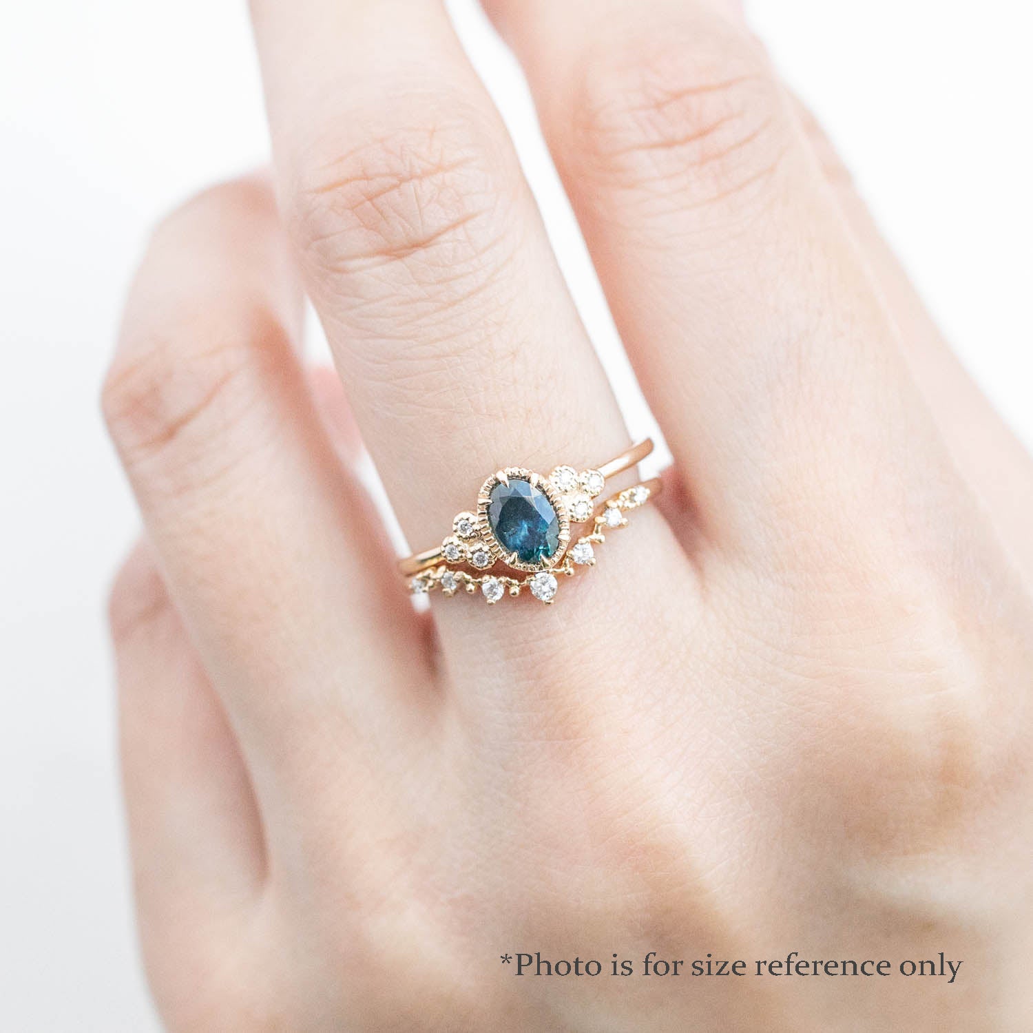 Celine Ring featuring a 0.60ct teal-blue Montana sapphire in a 14k yellow gold with six natural diamond accents on a hand with a stacking diamond band on a hand