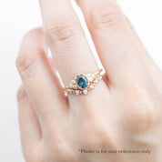 Celine Ring featuring a 0.60ct teal-blue Montana sapphire in a 14k yellow gold with six natural diamond accents on a hand with a stacking diamond band on a hand