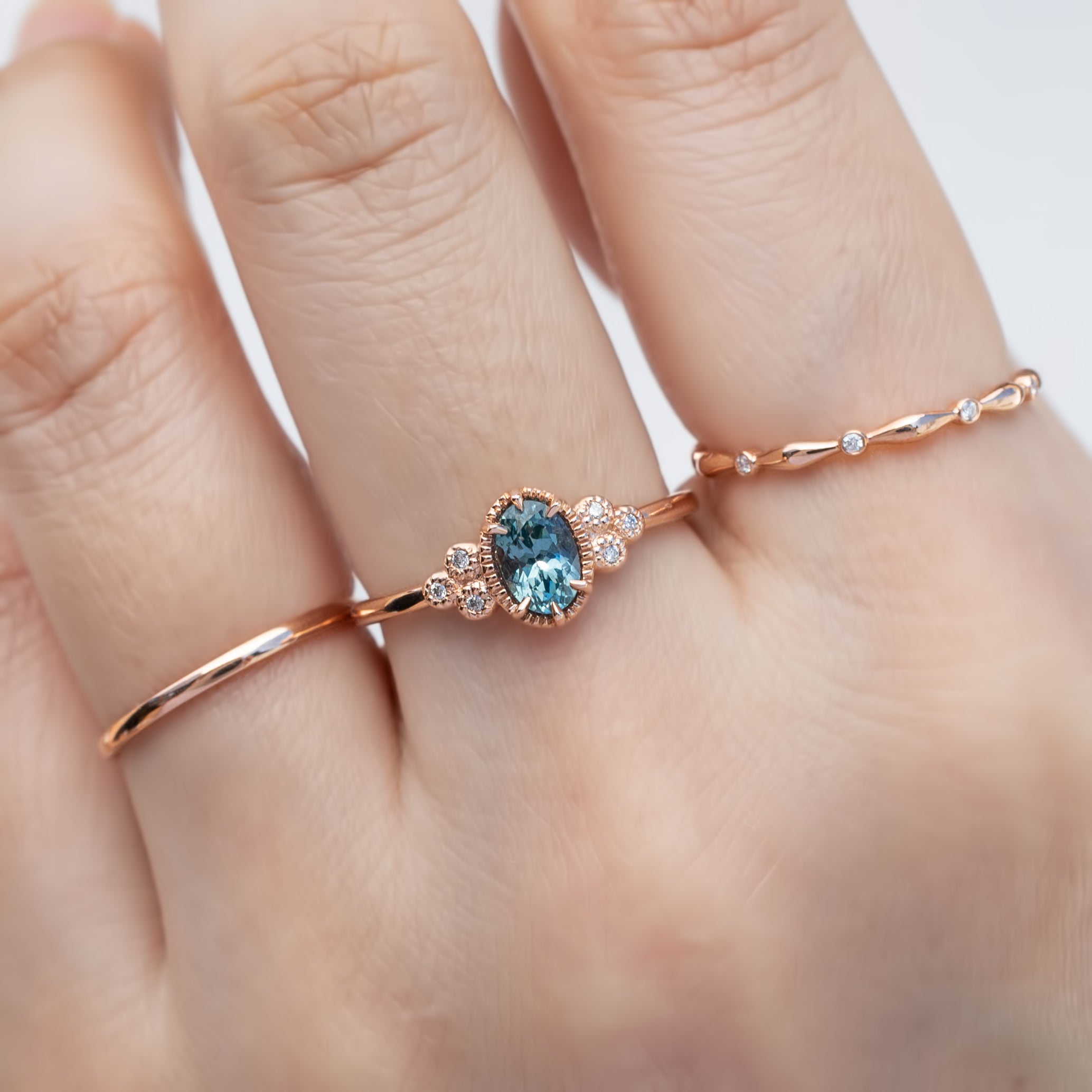 Celine Ring featuring a 0.60ct teal-blue Montana sapphire in a 14k rose gold with six natural diamond accents on a hand