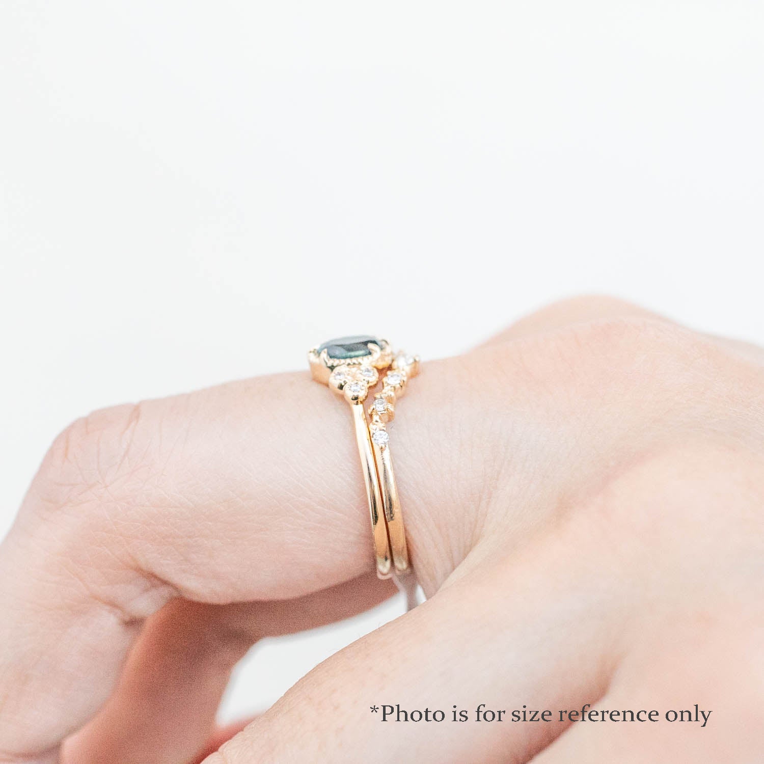 Celine Ring featuring a 0.60ct teal-blue Montana sapphire in a 14k yellow gold with six natural diamond accents on a hand showing side view with a band