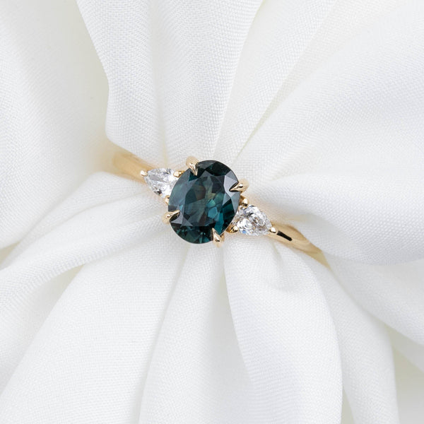 Gold ring with a green gemstone and smaller diamonds on a white fabric background